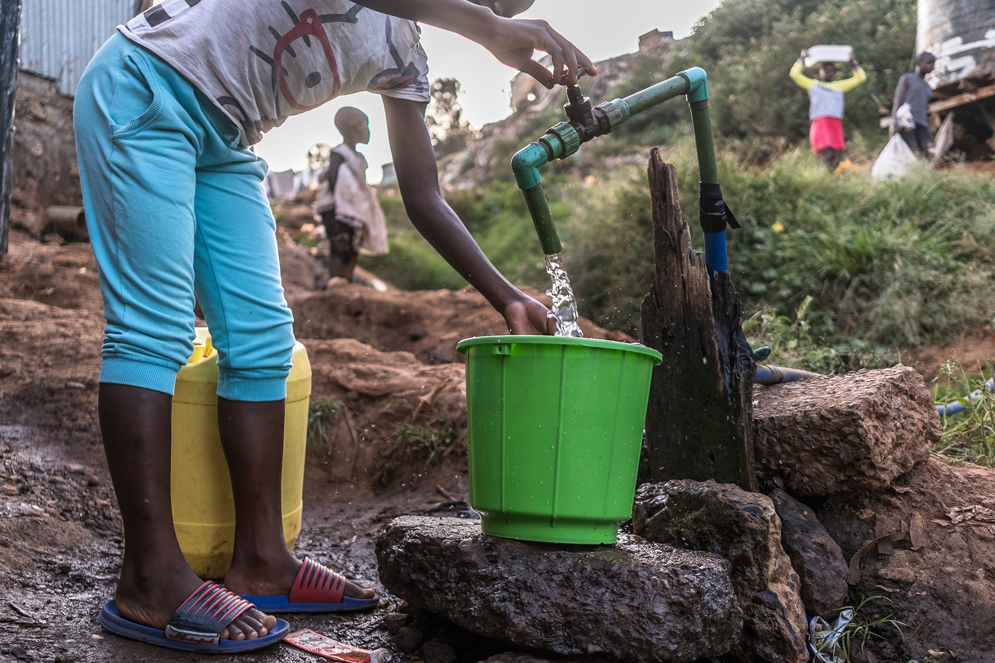 child filling a bucket from an outside tap
