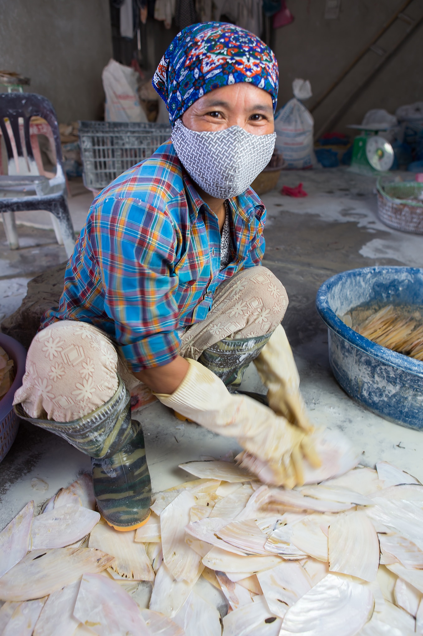 person squatting to sort through seashells in a factory